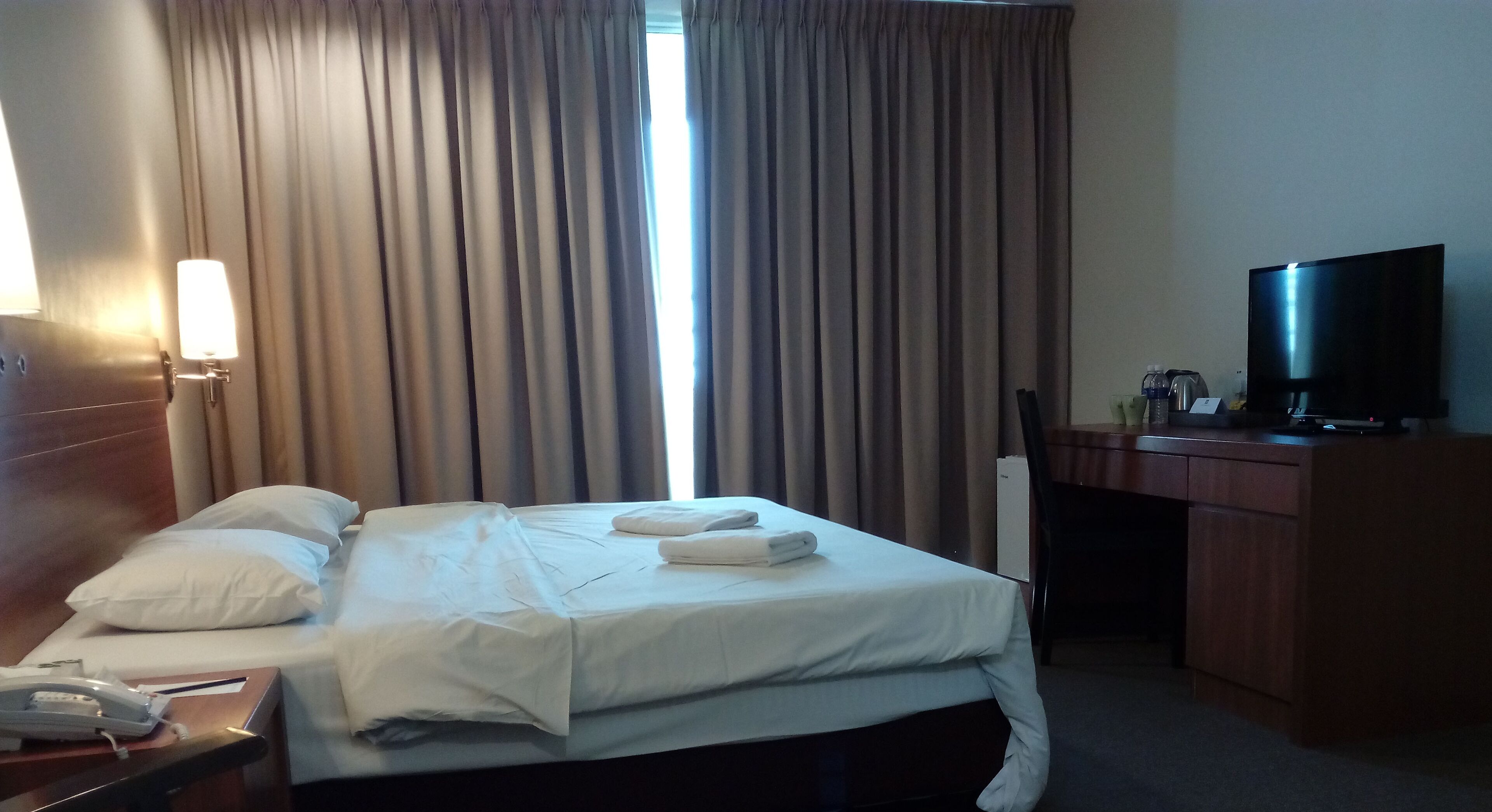Habitación de hotel con cama, escritorio, televisor y lámpara.
