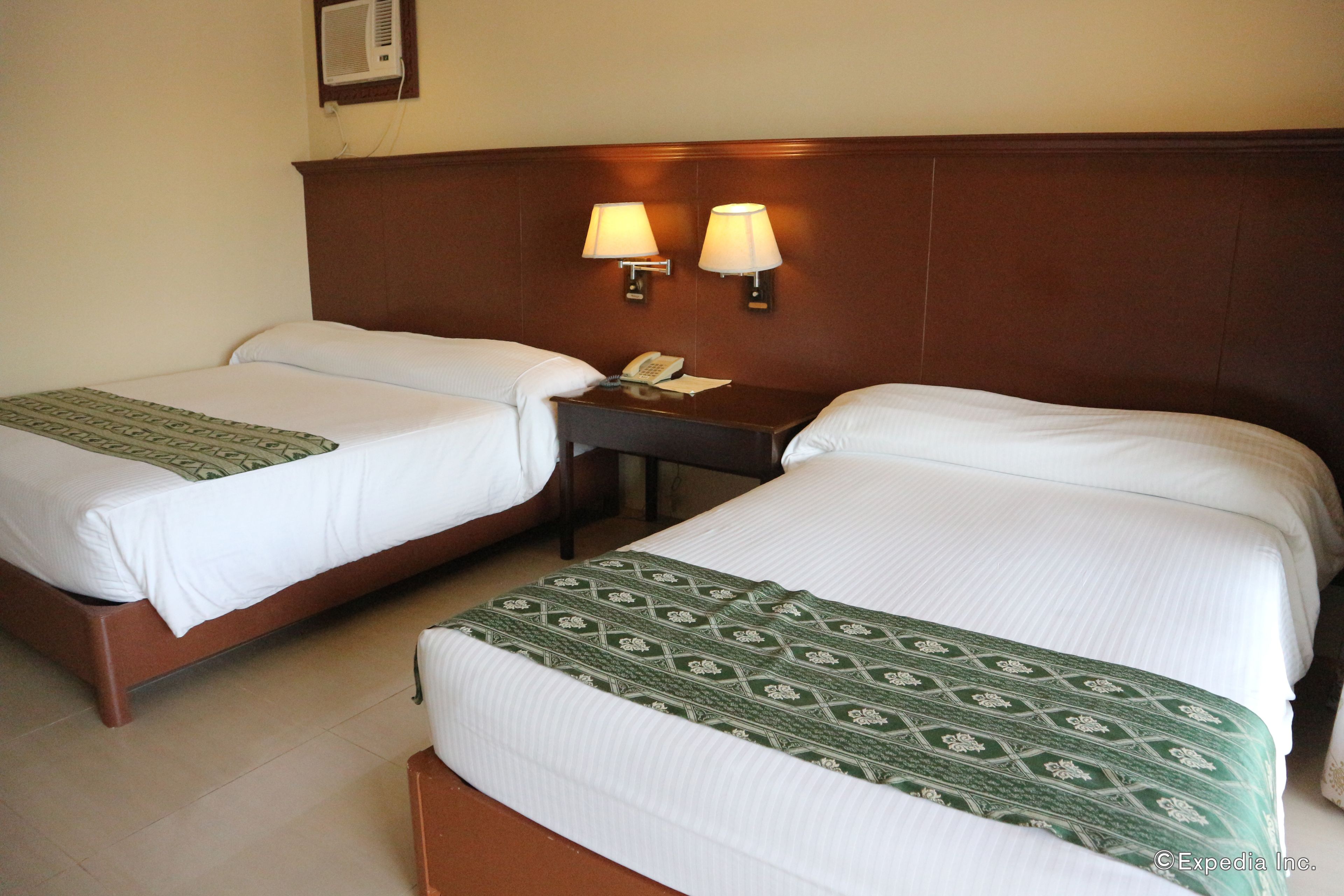 A hotel room with two single beds, a nightstand with a telephone, and two wall-mounted lamps.