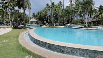 A large, curved swimming pool surrounded by palm trees and a stone wall.
