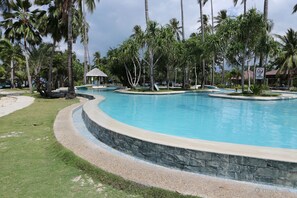 Una gran piscina curva rodeada de palmeras y un muro de piedra.