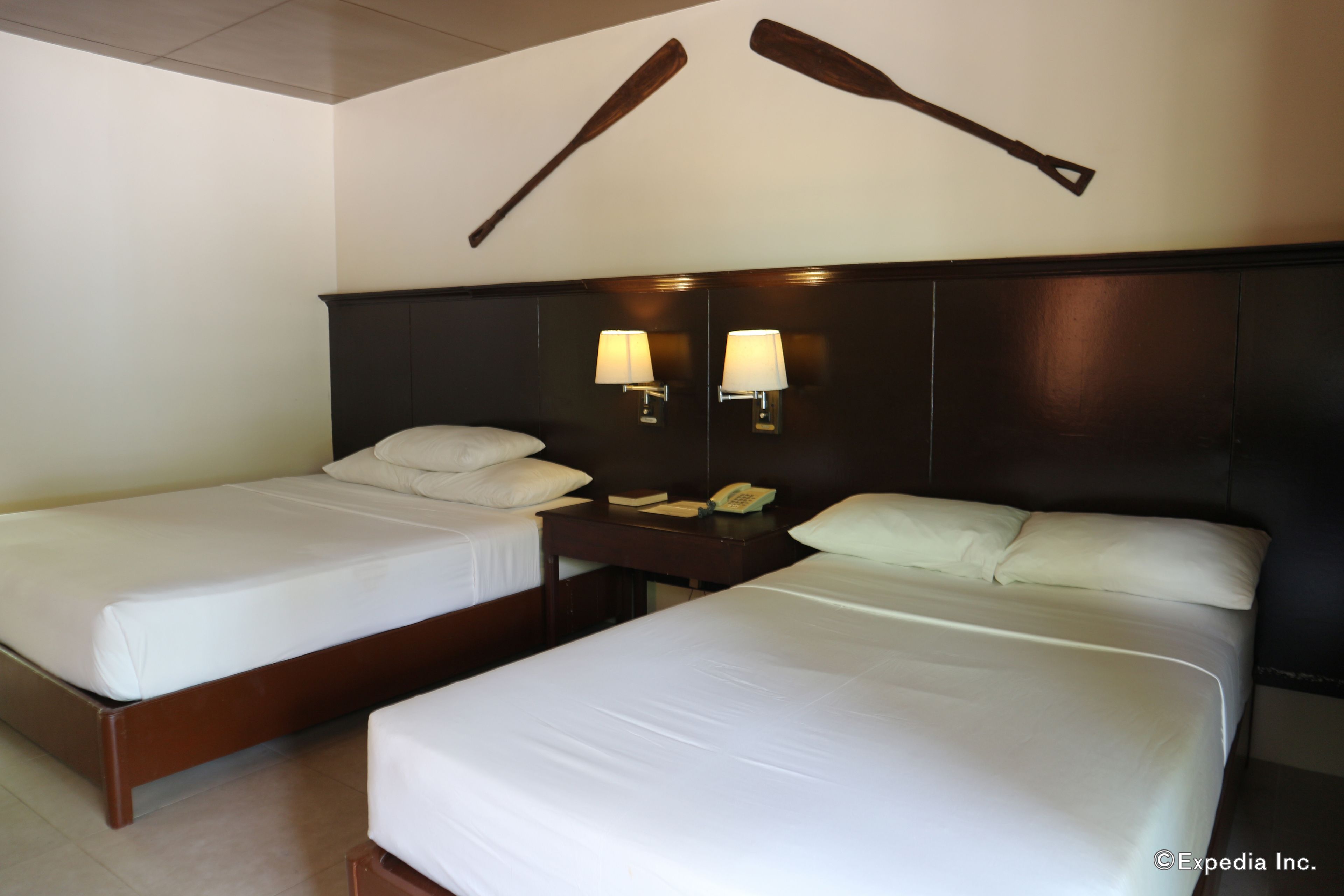 A hotel room with two beds, a wooden headboard, two wall-mounted lamps, and a telephone on the nightstand.