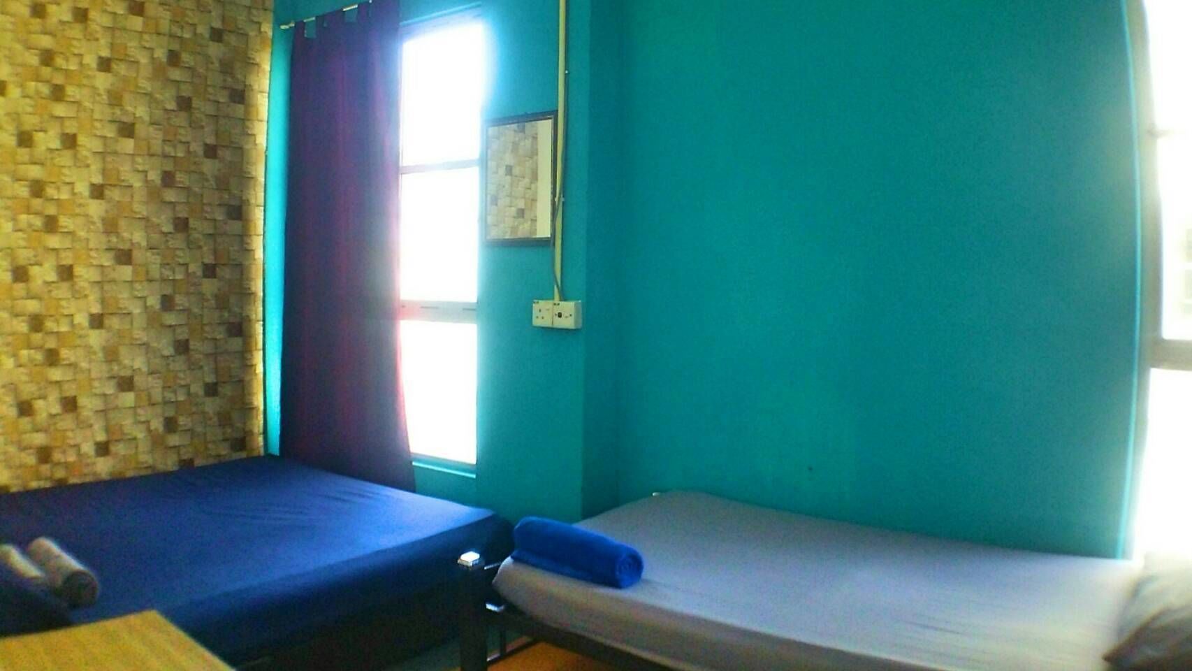 A room with two single beds, a window with curtains, a wall-mounted light switch, and a tiled wall.