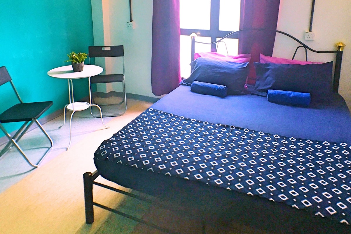 Un dormitorio con una cama, una silla, una mesita y una ventana con cortinas.