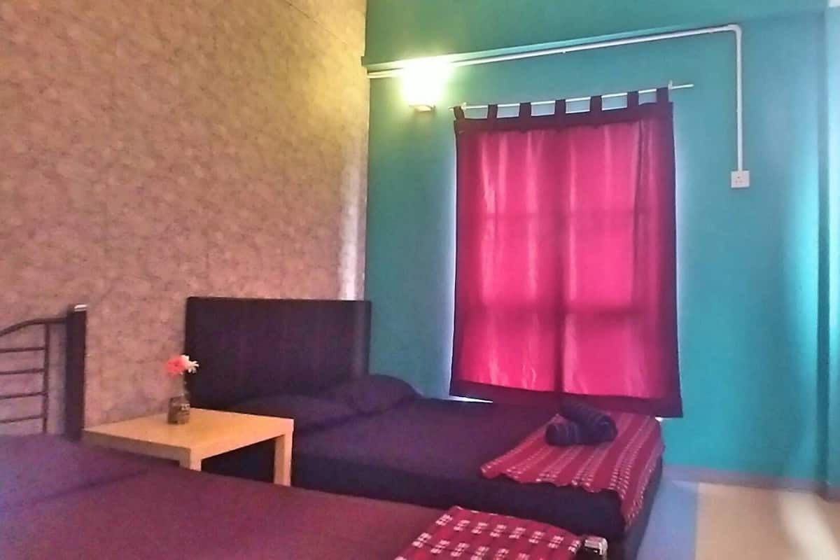 Una habitación con cama, una mesita con un florero, una cortina roja y una lámpara fijada a la pared.