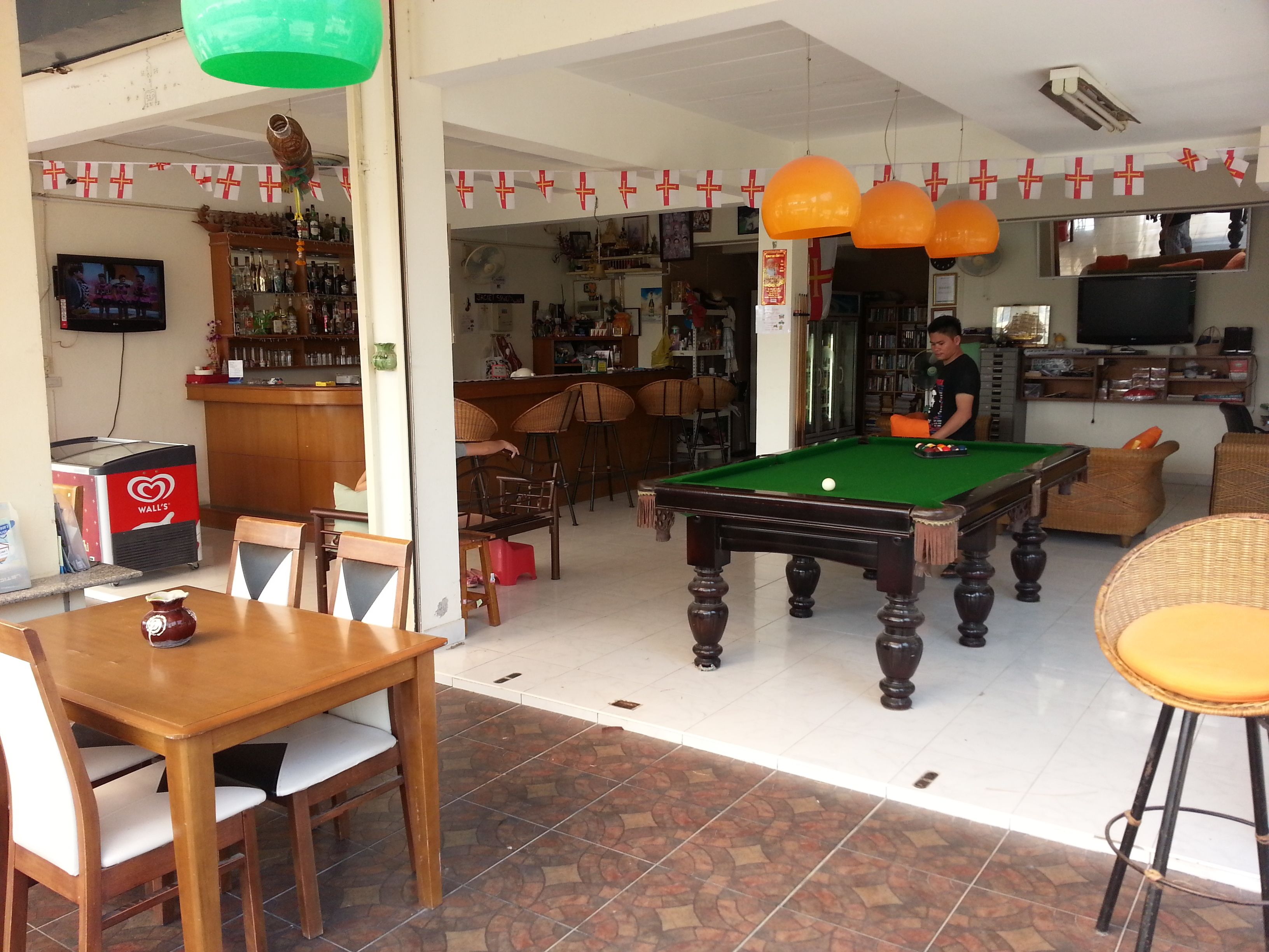 A billiards table in a room with a bar area, chairs, and a television.