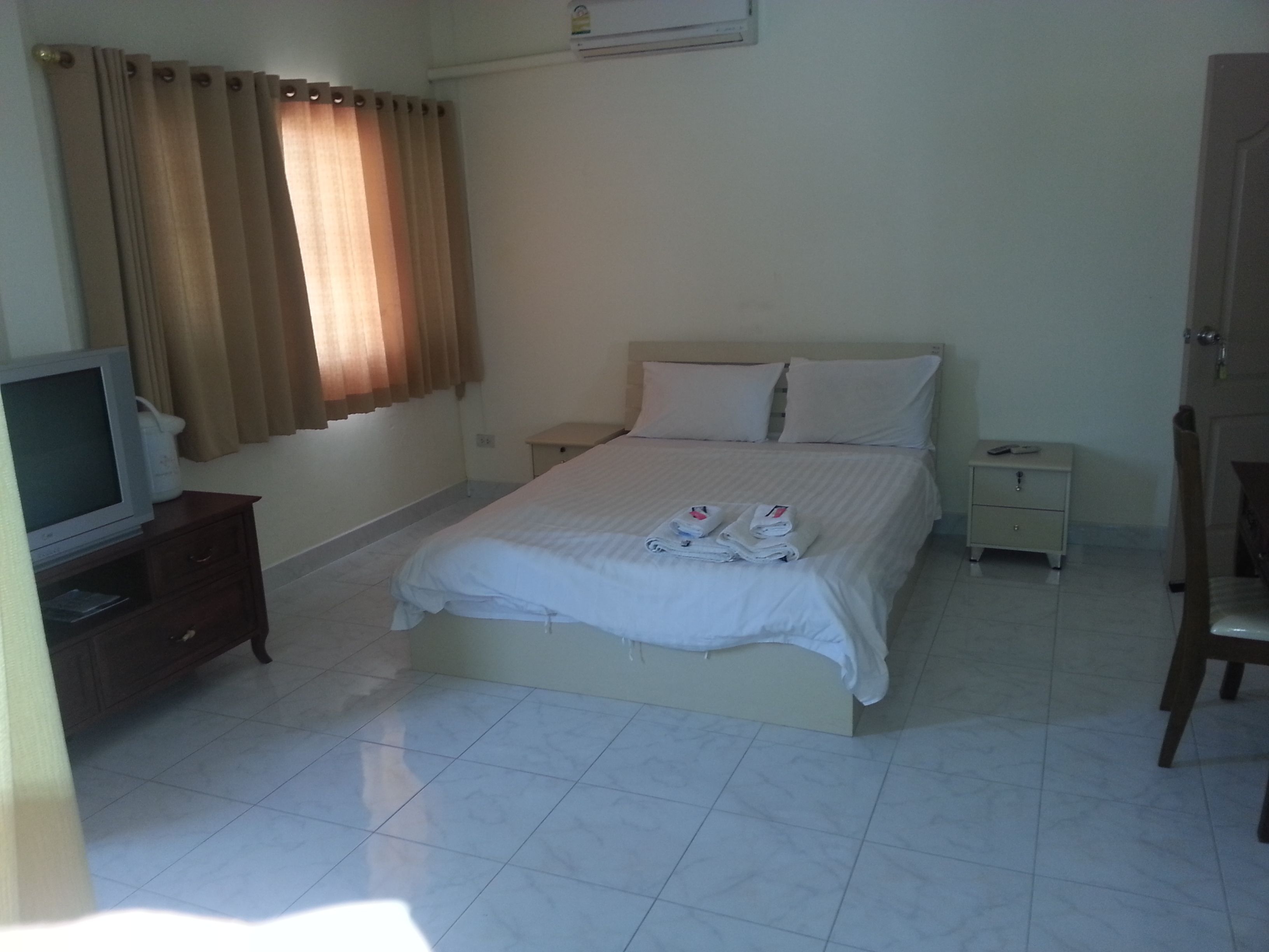 Una habitación de hotel con una cama, un televisor en un soporte, una mesita de noche, una silla y un armario.