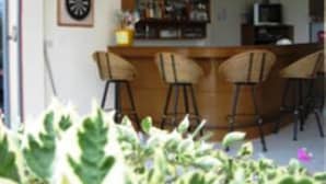 Uma área de bar com balcão e banquetas, um relógio na parede e uma estante de livros ao fundo.