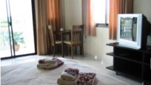Quarto de hotel com cama, televisão em suporte, uma cadeira e uma mesa.