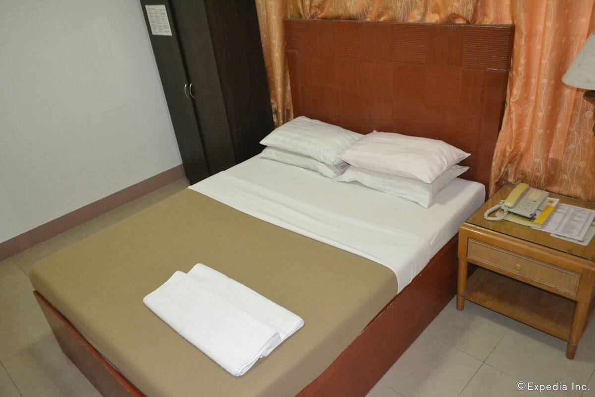 A neatly made bed with white linens and a folded white towel on the bed.