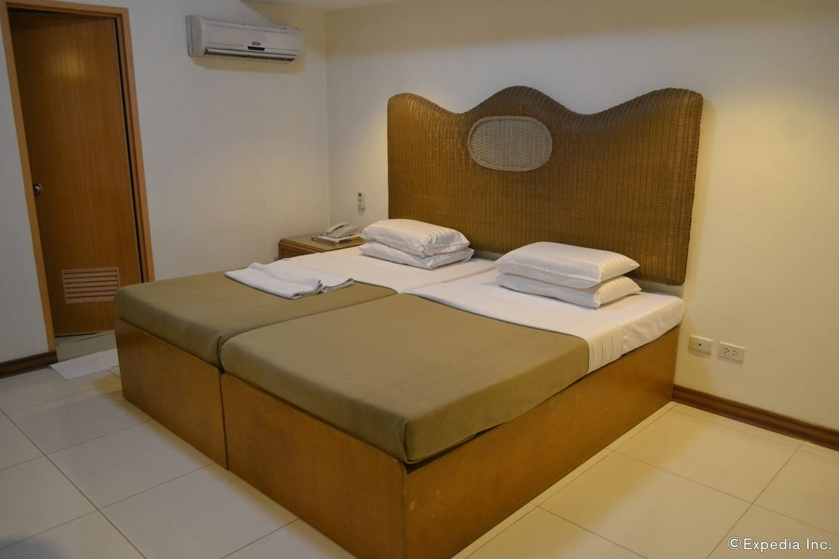 A hotel room with a double bed, a wooden headboard, a bedside table with a lamp, and a wall-mounted air conditioner.
