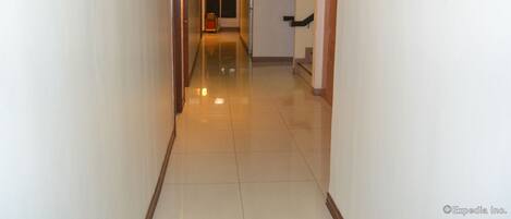A hotel hallway with a polished floor, a trash bin, and a door at the end.