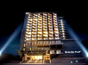Un hotel moderno con una fachada geométrica singular, múltiples balcones y una entrada destacada con escalones que conducen a la recepción.