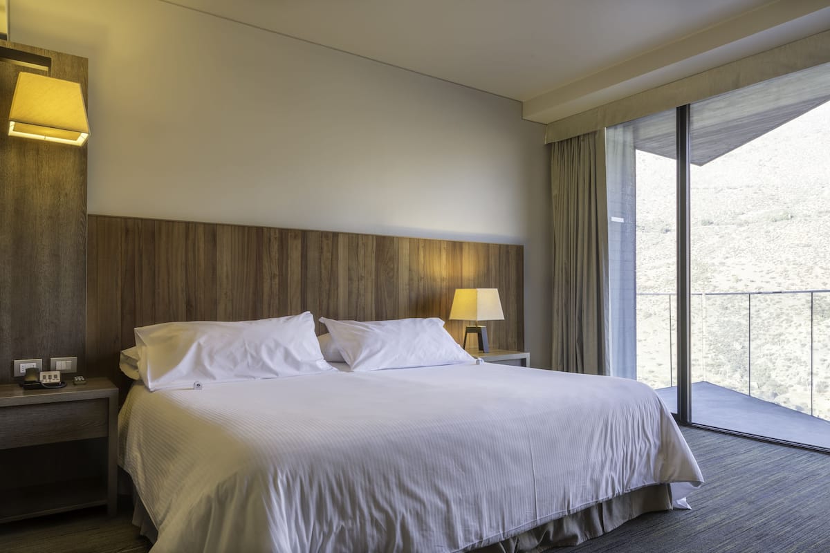 Ein Hotelzimmer mit einem großen Bett, zwei Nachttischen, einem Fenster mit Blick ins Freie.