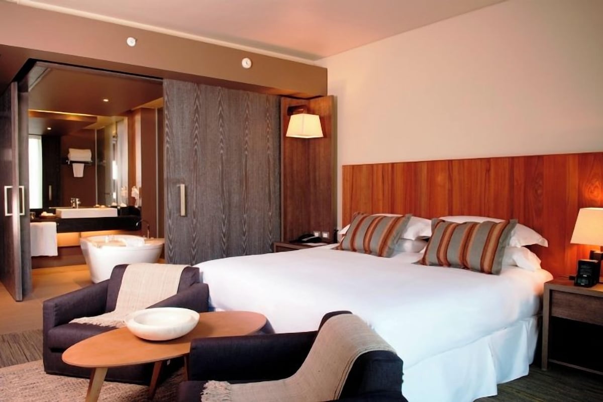 Een hotelkamer met een groot bed, een sofa, een kleintje tafeltje en een zichtbare badkamer door een open deur.