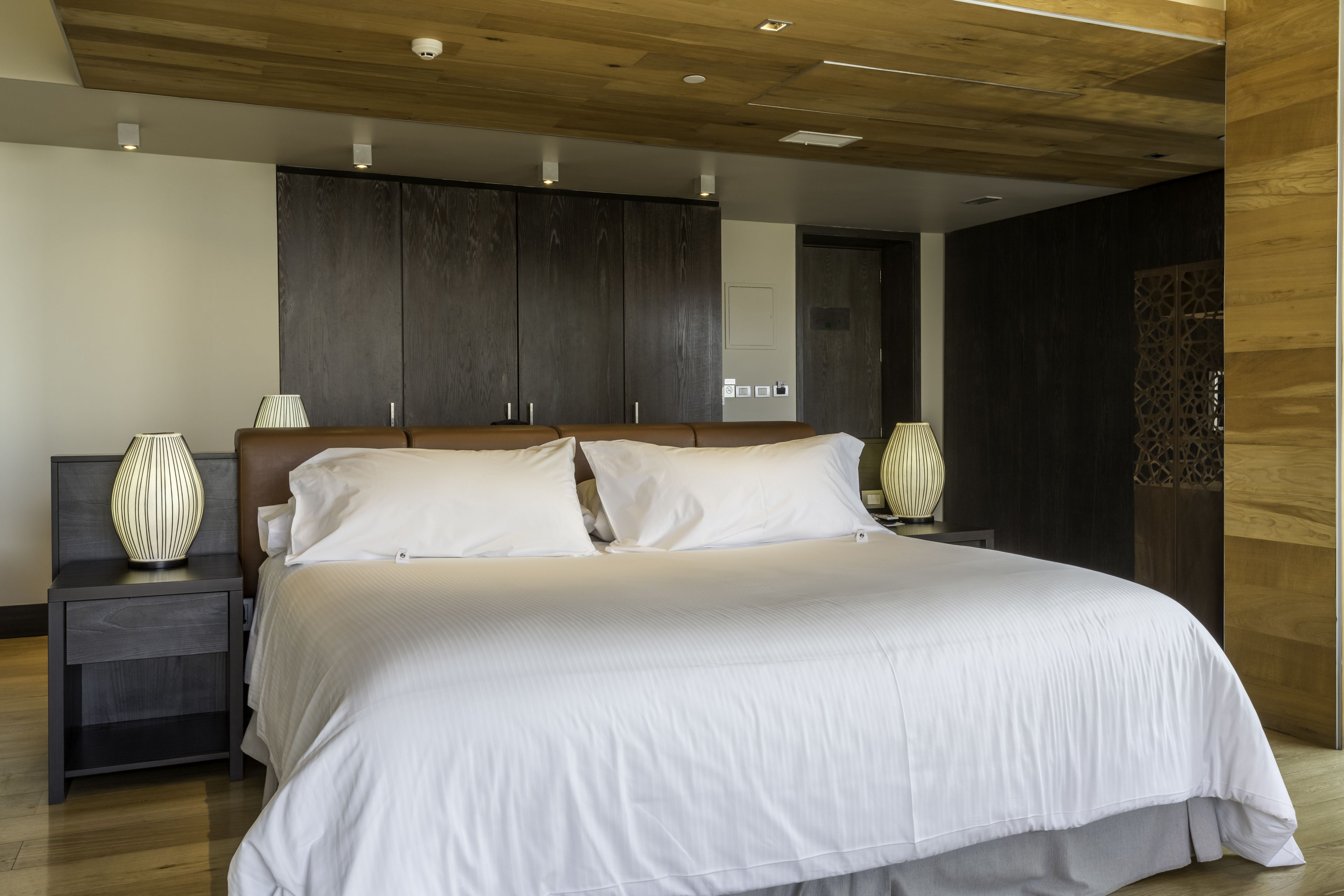 Ein modernes Schlafzimmer mit einem großen Bett, einem dunklen Holzschrank und einer dekorativen Wandverkleidung.