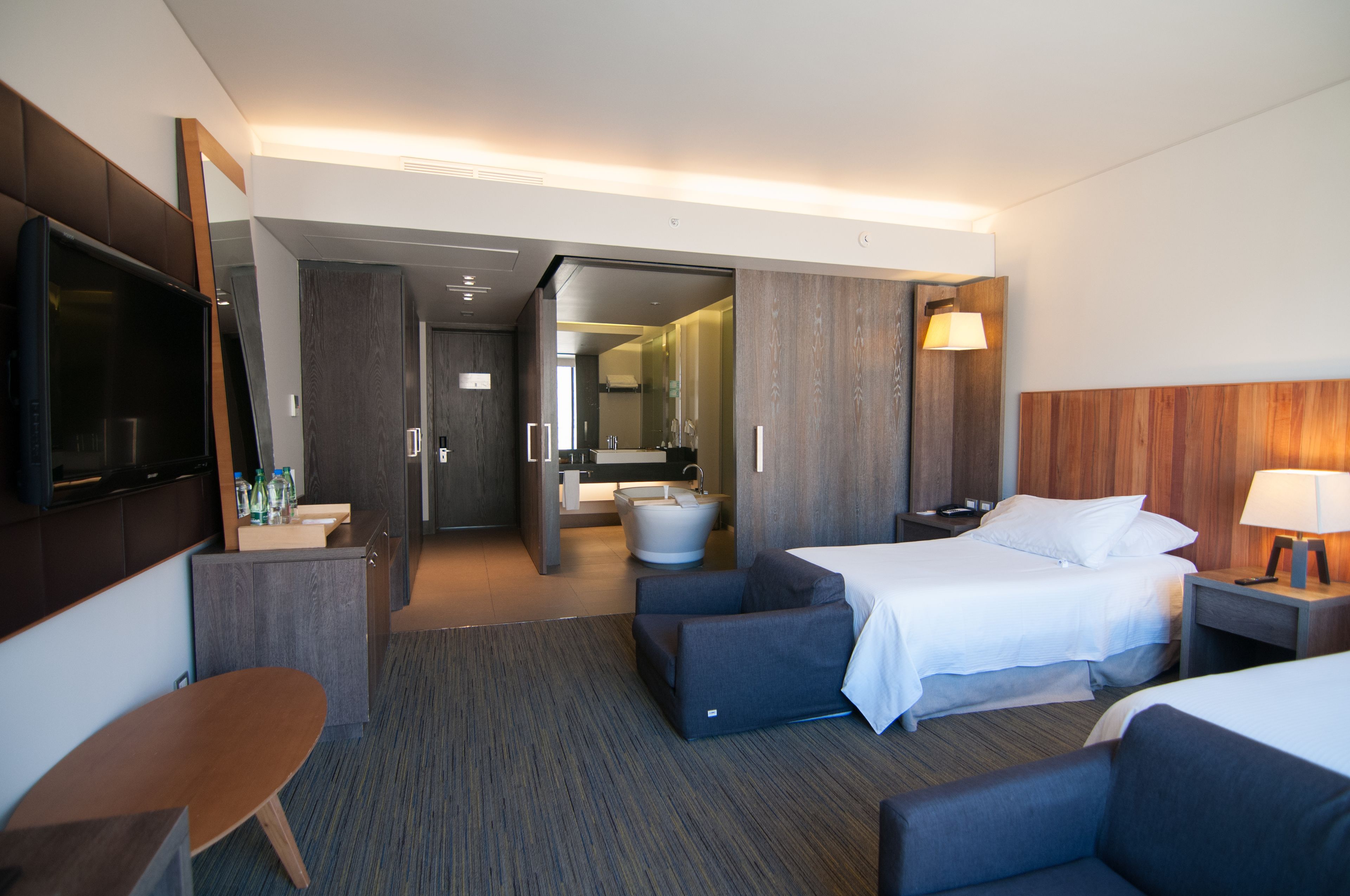 Habitación de hotel con dos camas, un escritorio, televisión, baño y espejo.