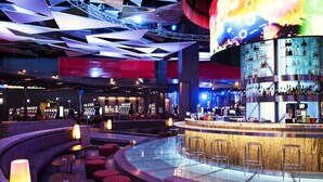 Eine moderne Bar mit einer gebogenen Sitzanordnung, einer zentralen Bar und einem großen, beleuchteten Bildschirm darüber.