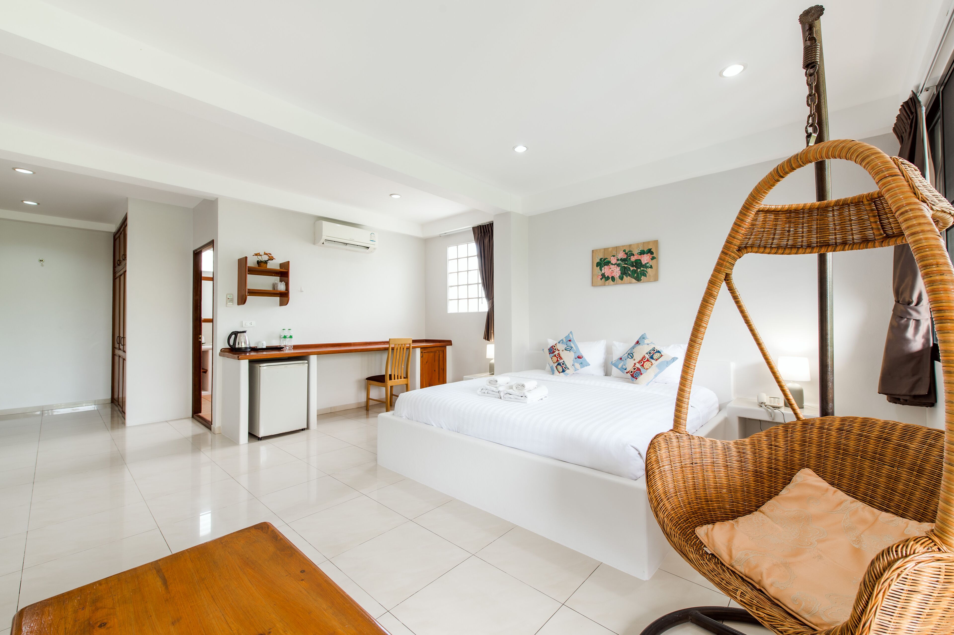 Une chambre d’hôtel avec un grand lit, un bureau, une chaise, un fauteuil suspendu et une petite kitchenette.