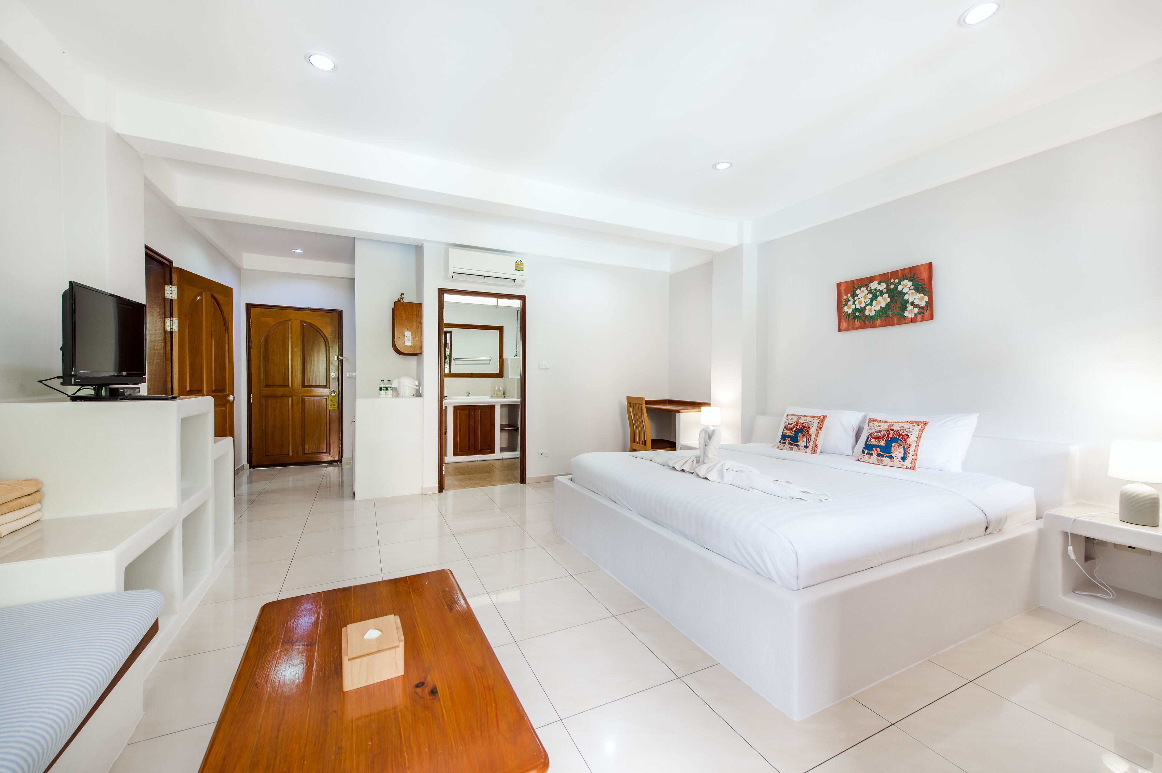 A modern hotel room with a large bed, a wooden coffee table, a television, and a bathroom visible through an open door.