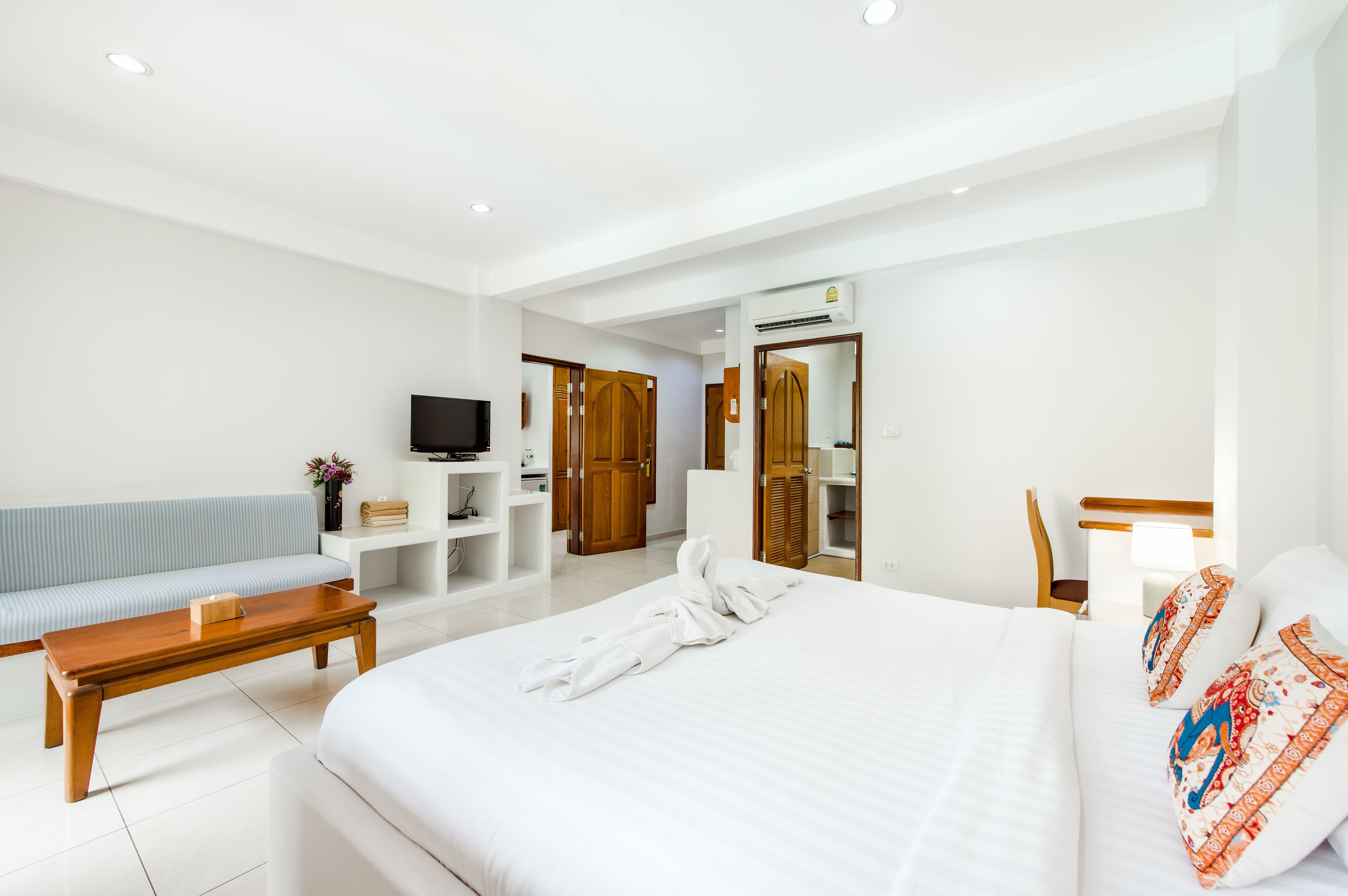 Une chambre d’hôtel avec un grand lit, un banc en bois, une télévision, une armoire et un miroir.