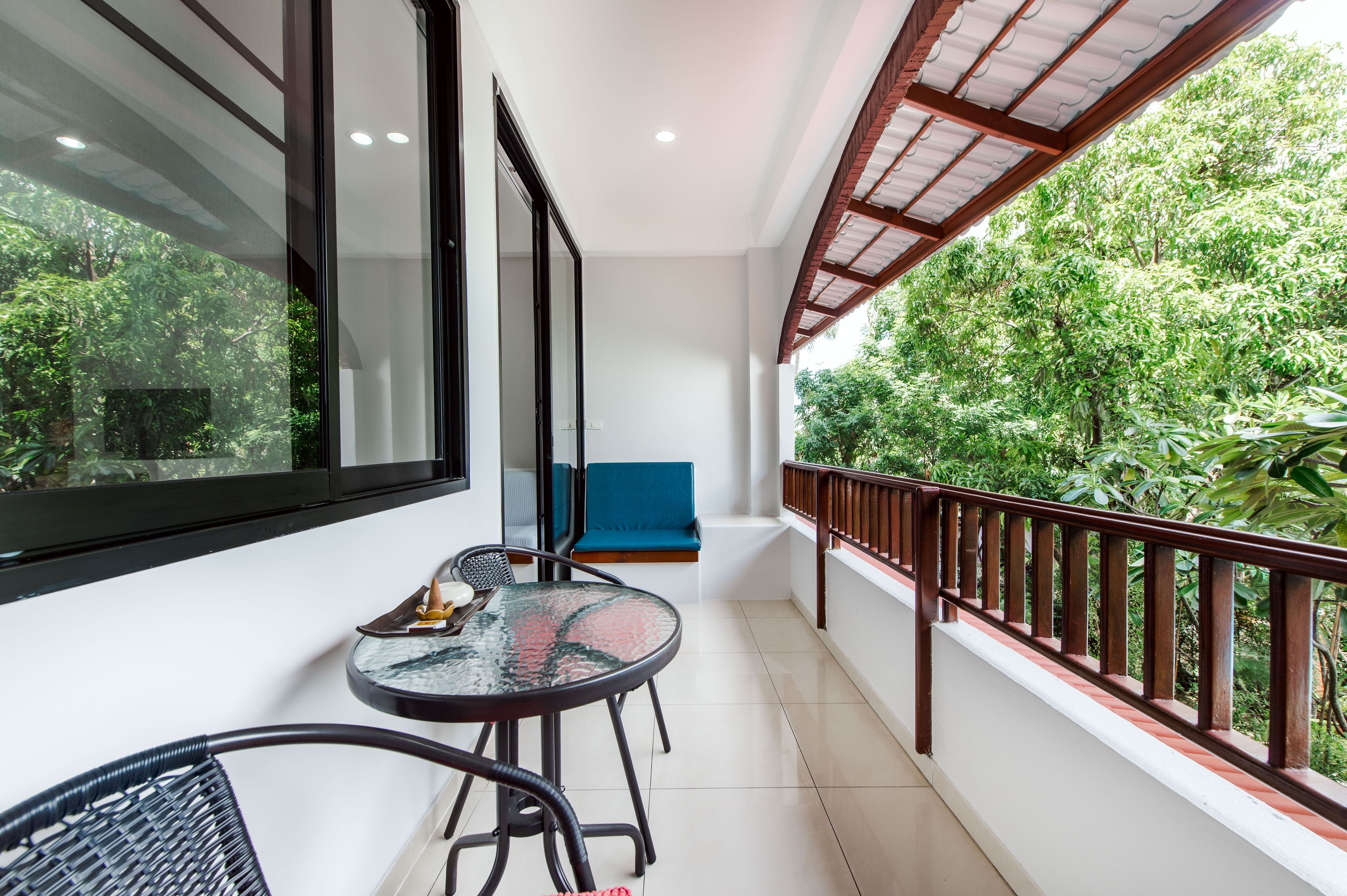 A balcony with a glass table, chairs, and a blue cushioned seat.