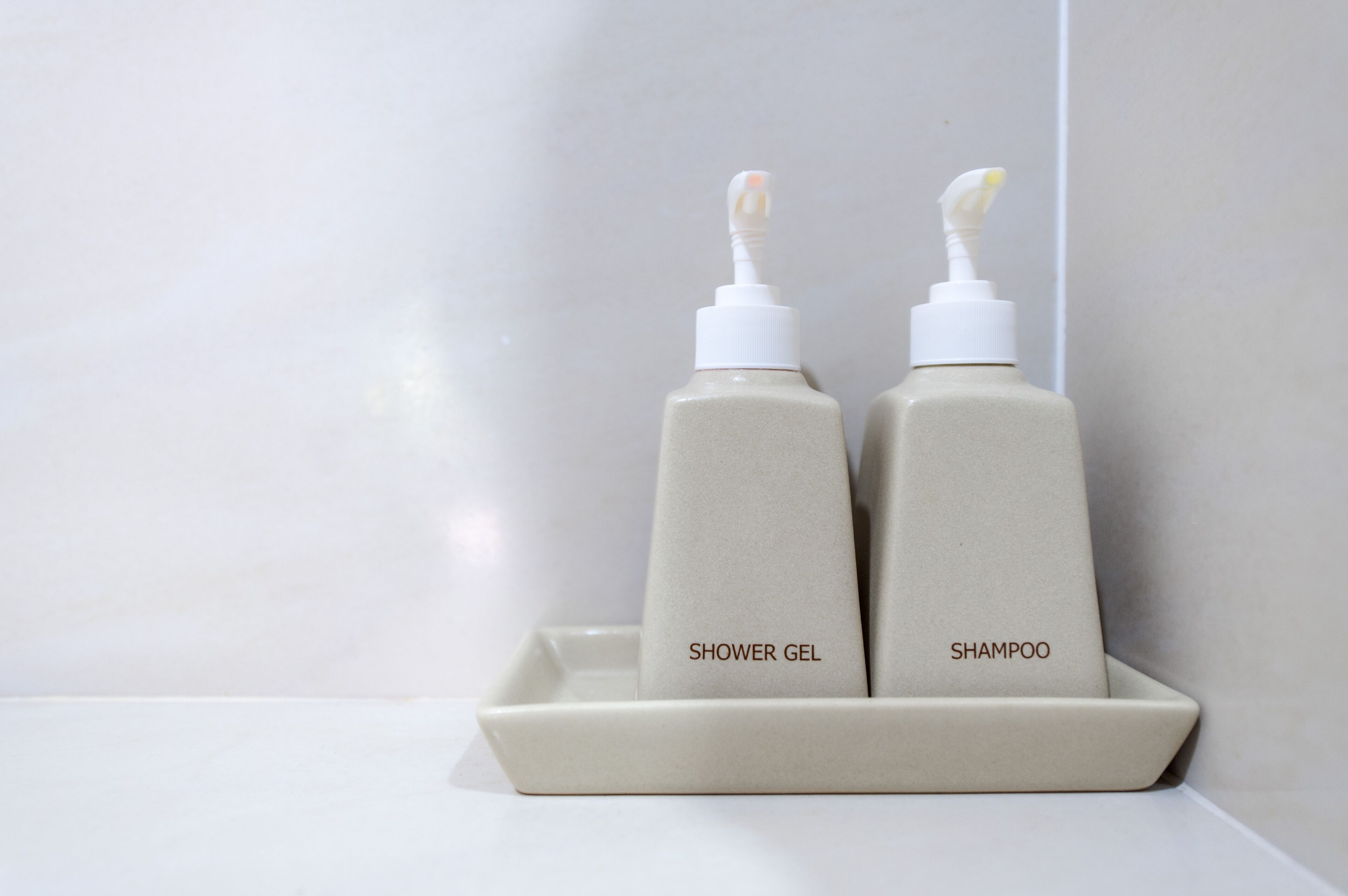 Deux flacons de produits de toilette étiquetés « gel douche » et « shampoing » sont posés sur un plateau blanc.