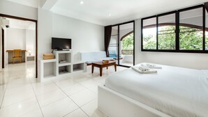 A modern hotel room with a large bed, a TV, a desk with a chair, and a balcony with a view of greenery. - Prinz Garden Villa Hua Hin (Hua Hin)