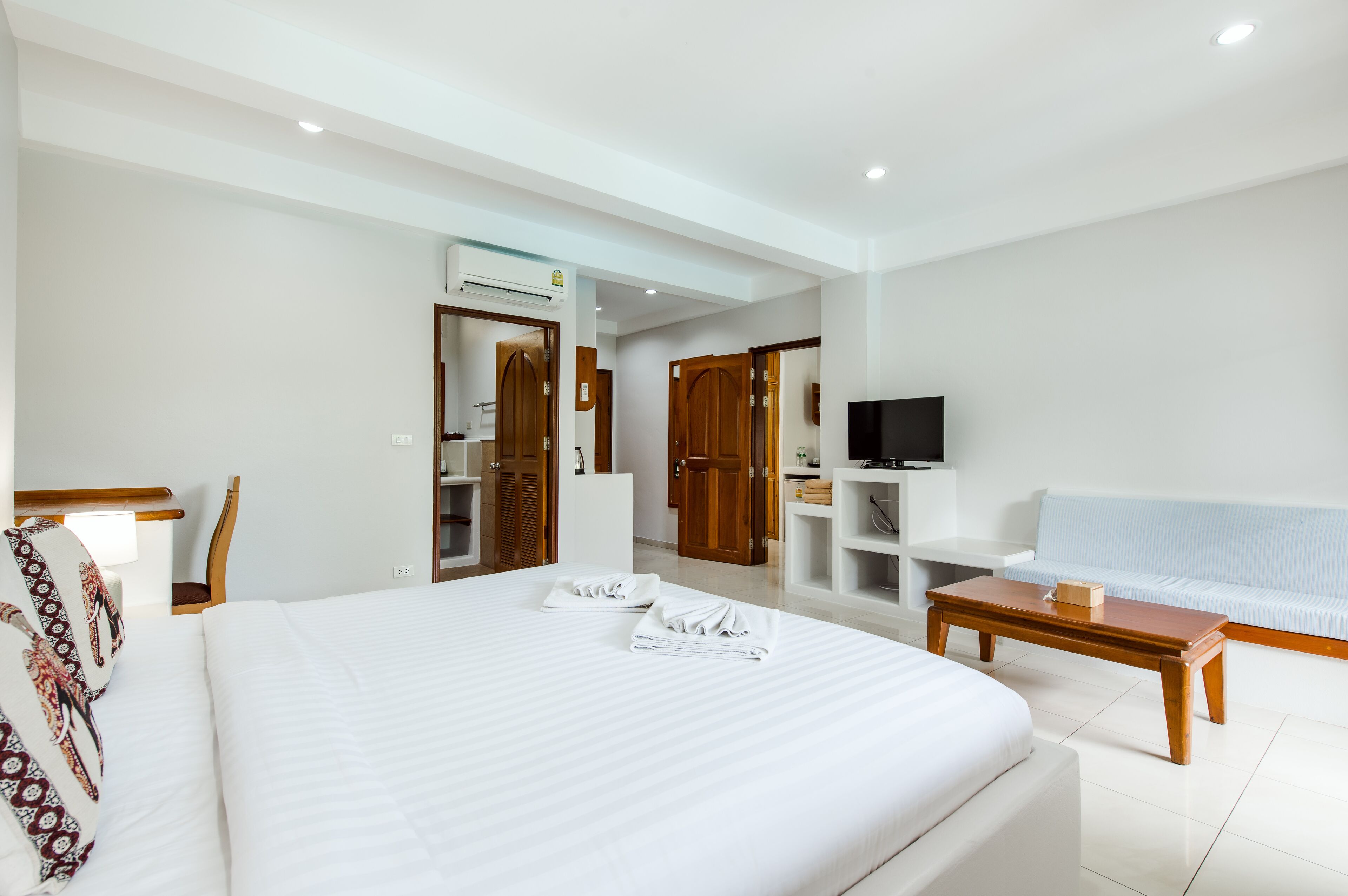 A hotel room with a large bed, a wooden coffee table, a white sofa, a TV, and a wardrobe.