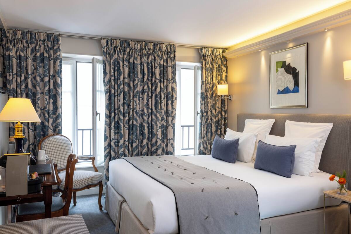 A hotel room with a large bed, a desk with a lamp, a chair, and a framed picture on the wall.