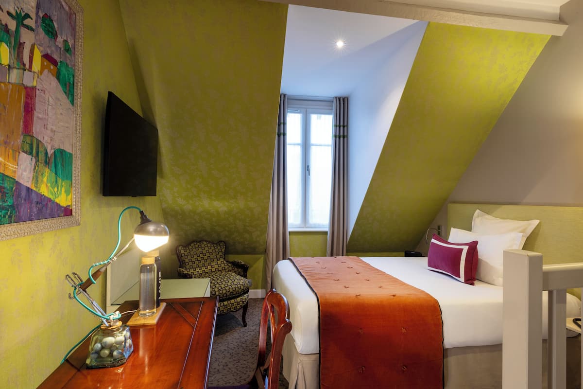 A room with a bed, a desk with a lamp, a chair, and a window with curtains.