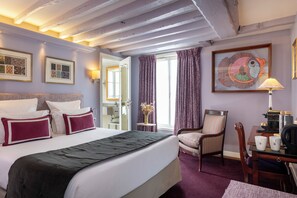 A hotel room with a bed, a chair, a table, a lamp, and artwork on the wall. - Le Relais des Halles (Paris)