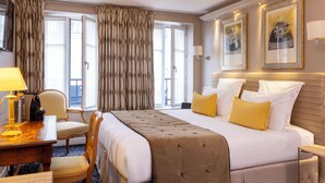 A hotel room with a large bed, a desk with a lamp, a chair, and a window with curtains. - Le Relais des Halles (Paris)