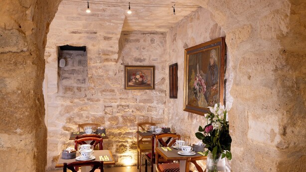 A rustic dining area with stone walls, wooden tables, and chairs. There are framed artworks on the walls and a vase with flowers on the table. - Le Relais des Halles (Paris)