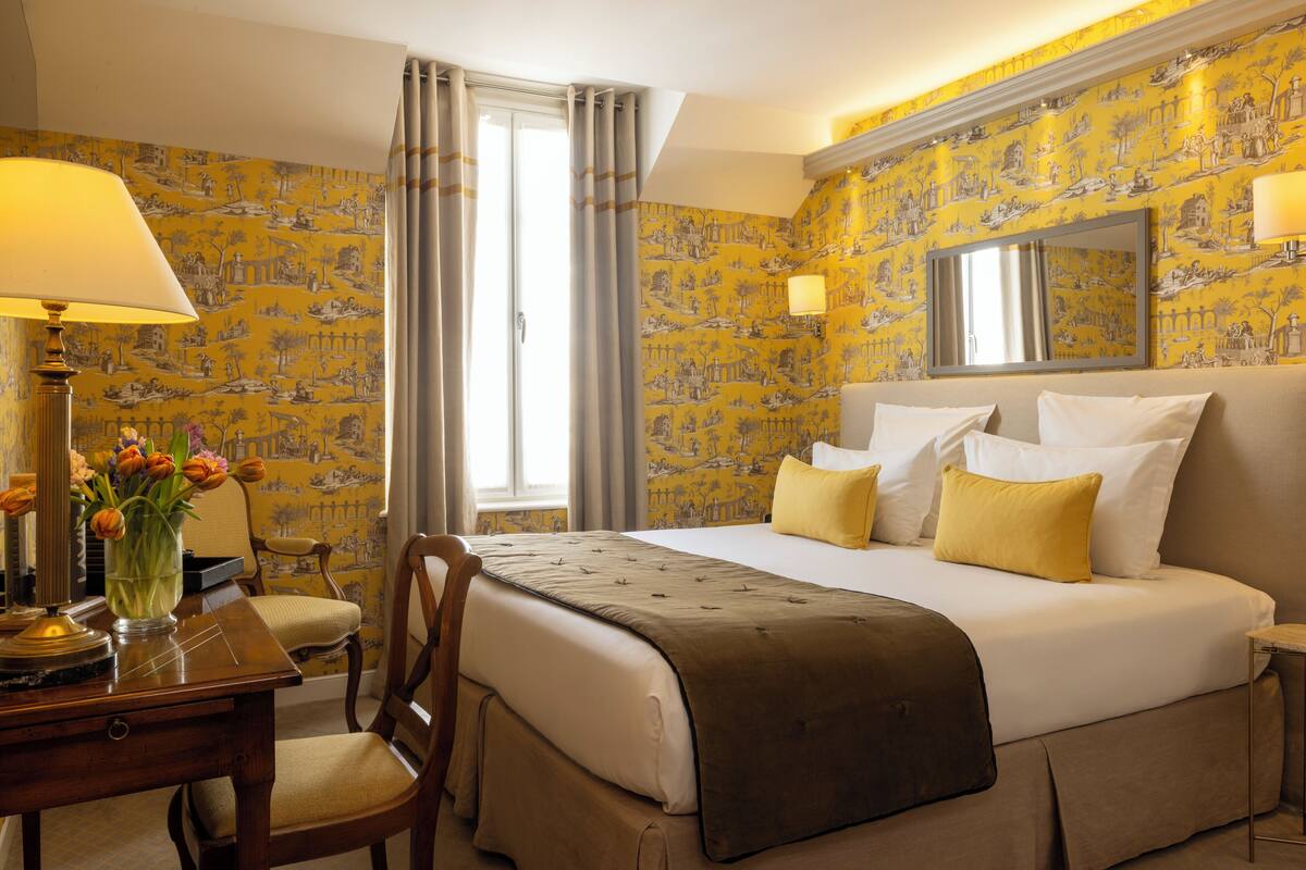 A hotel room with a large bed, a desk with a lamp, a chair, and a vase of flowers.
