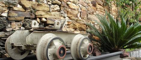 A model tank on a track with a stone wall and greenery in the background.