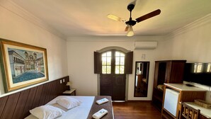 A hotel room with a bed, a desk, a television, and a painting on the wall. - Pousada Casa dos Contos (Ouro Preto)