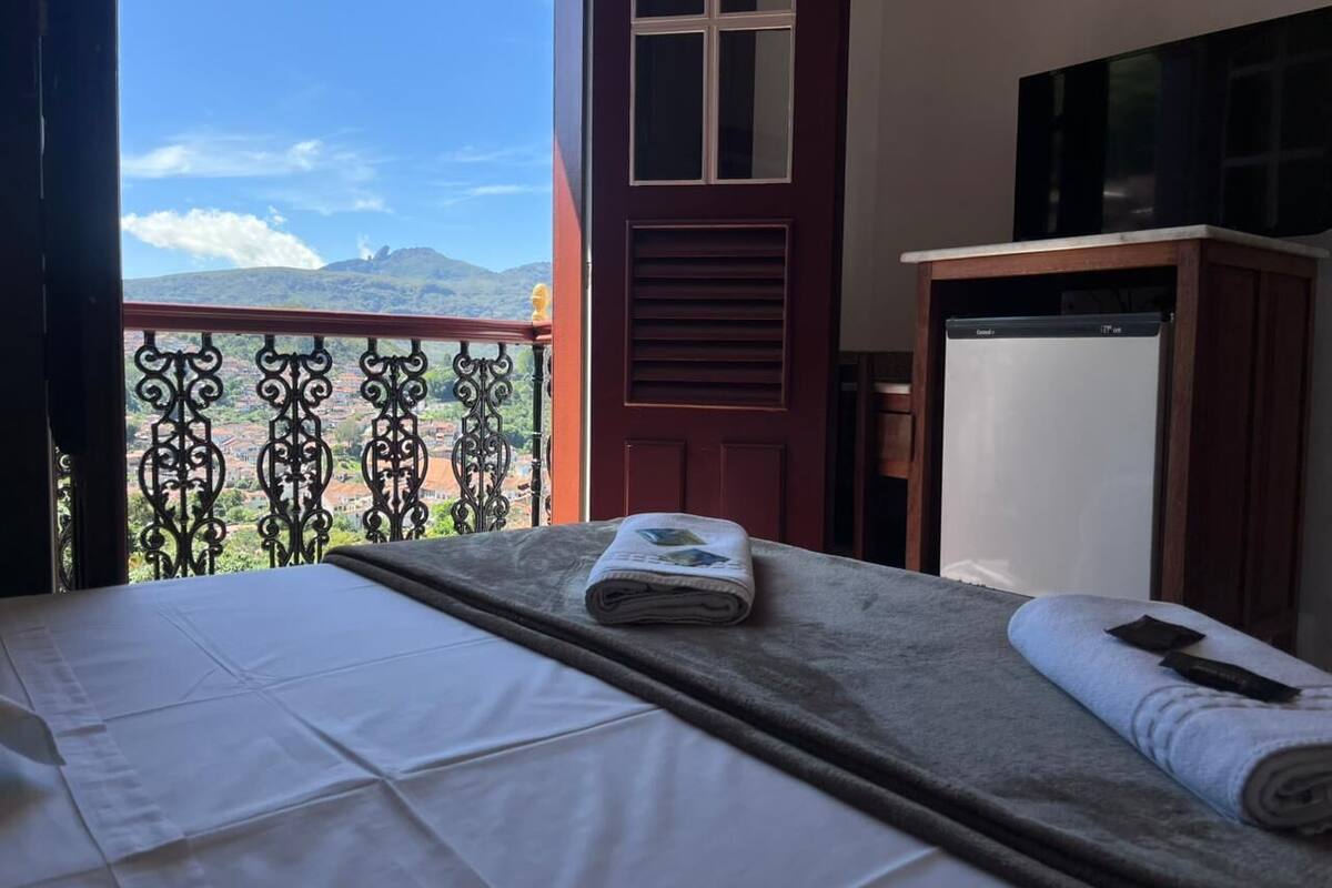 Habitación de hotel con cama, balcón y vistas a montañas, además de un televisor.