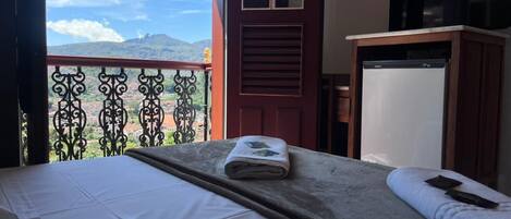 A hotel room with a bed, a balcony with a view of mountains, and a television.