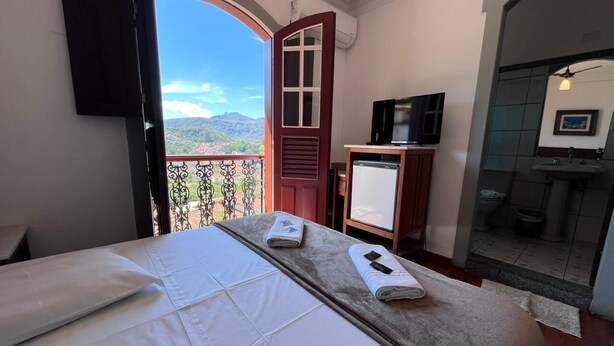 A hotel room with a bed, a TV, a small desk, and a bathroom visible through an open door. - Pousada Casa dos Contos (Ouro Preto)