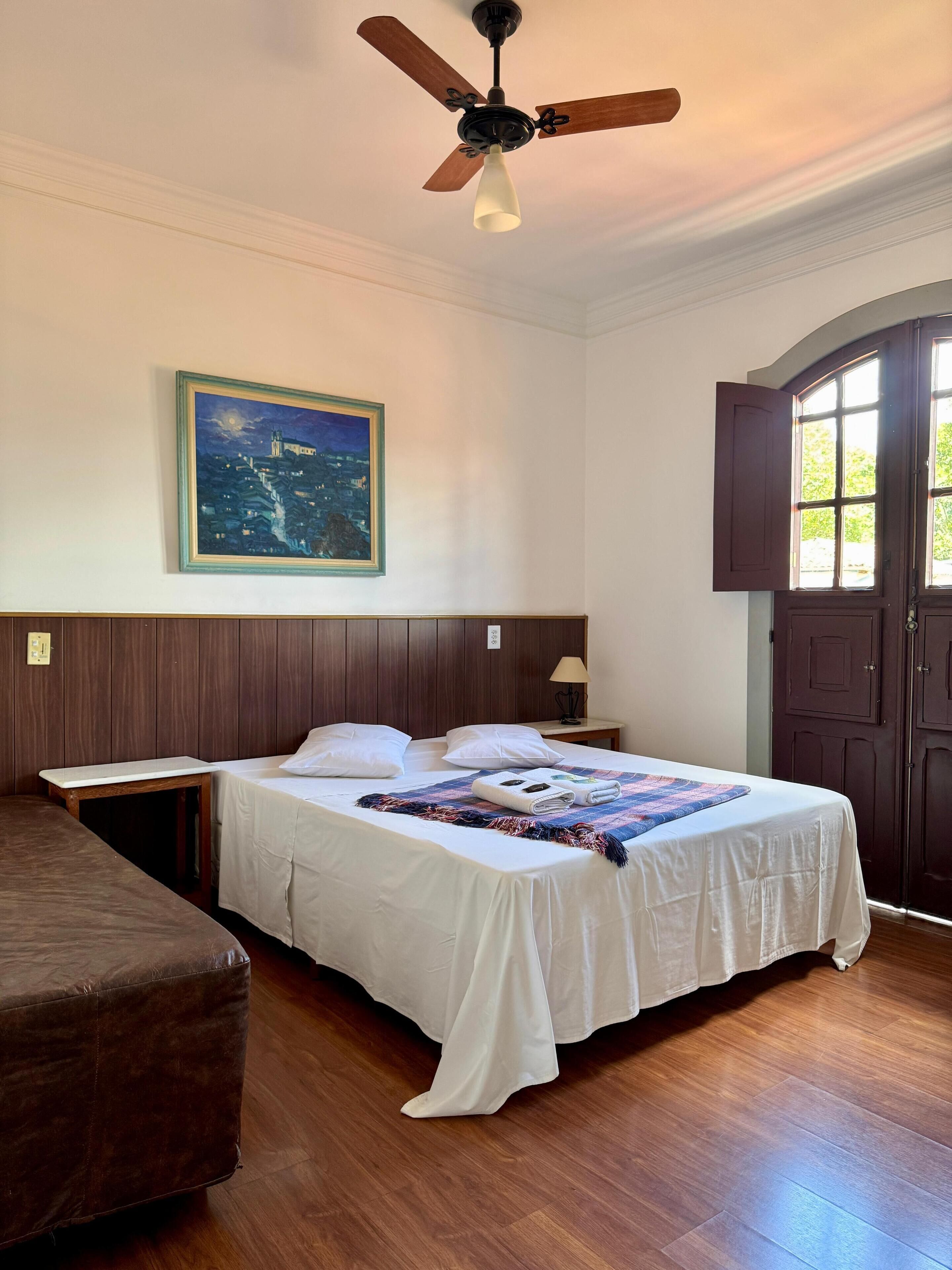 A hotel room with a bed, a nightstand, a lamp, a painting, and a door.