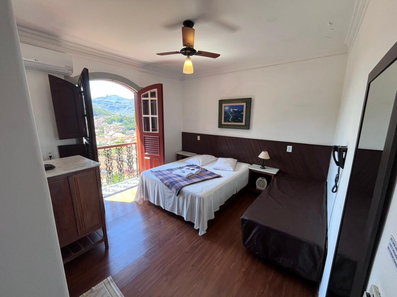 Un dormitorio con cama, mesita de noche, ventilador de techo y vistas al exterior.