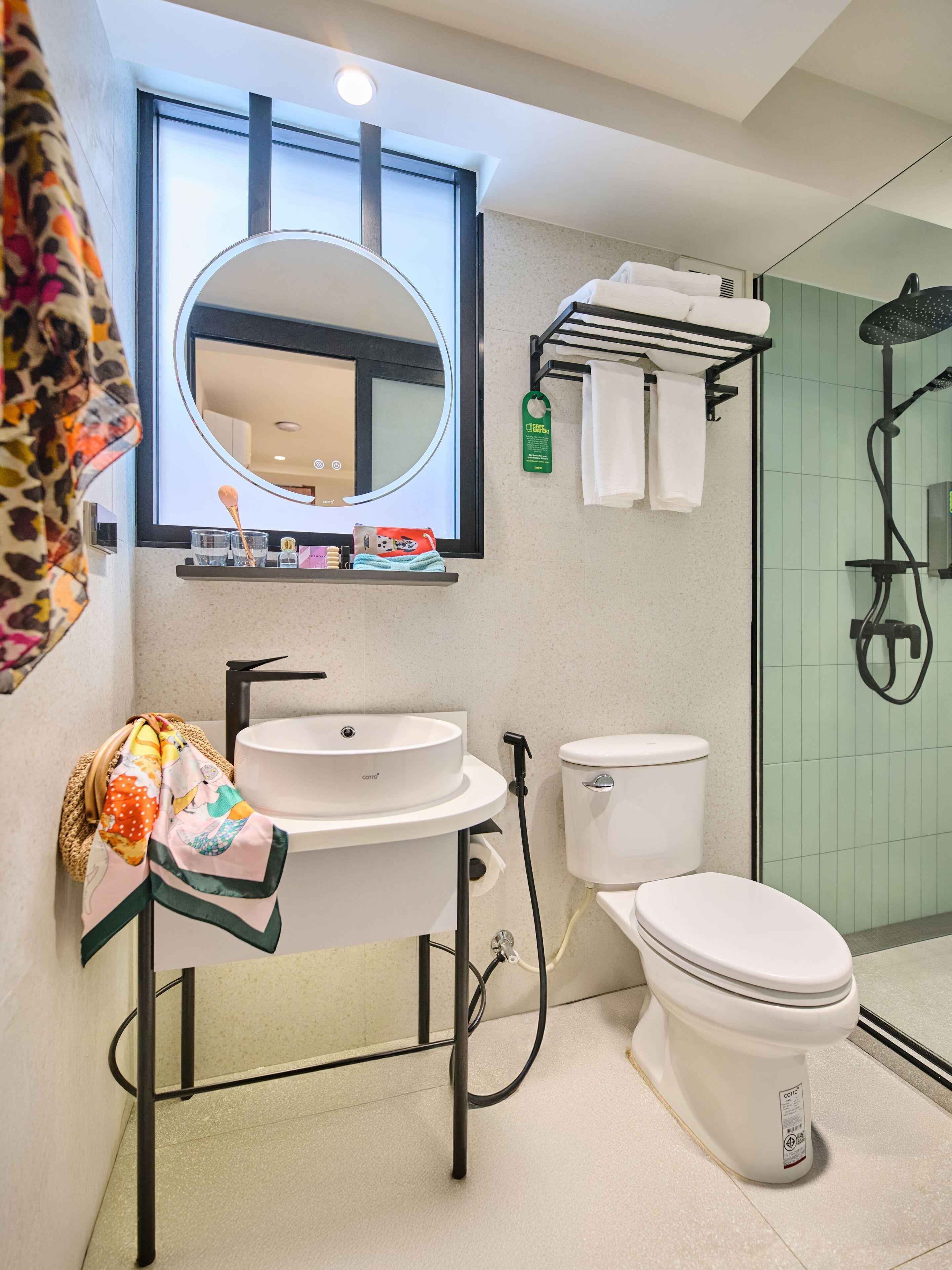 A modern bathroom with a round mirror, white sink, toilet, and shower area.