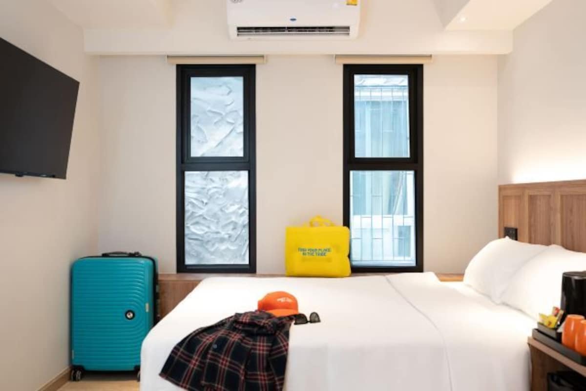 Una habitación de hotel con una cama, una maleta, un bolso amarillo y un televisor montado en la pared.