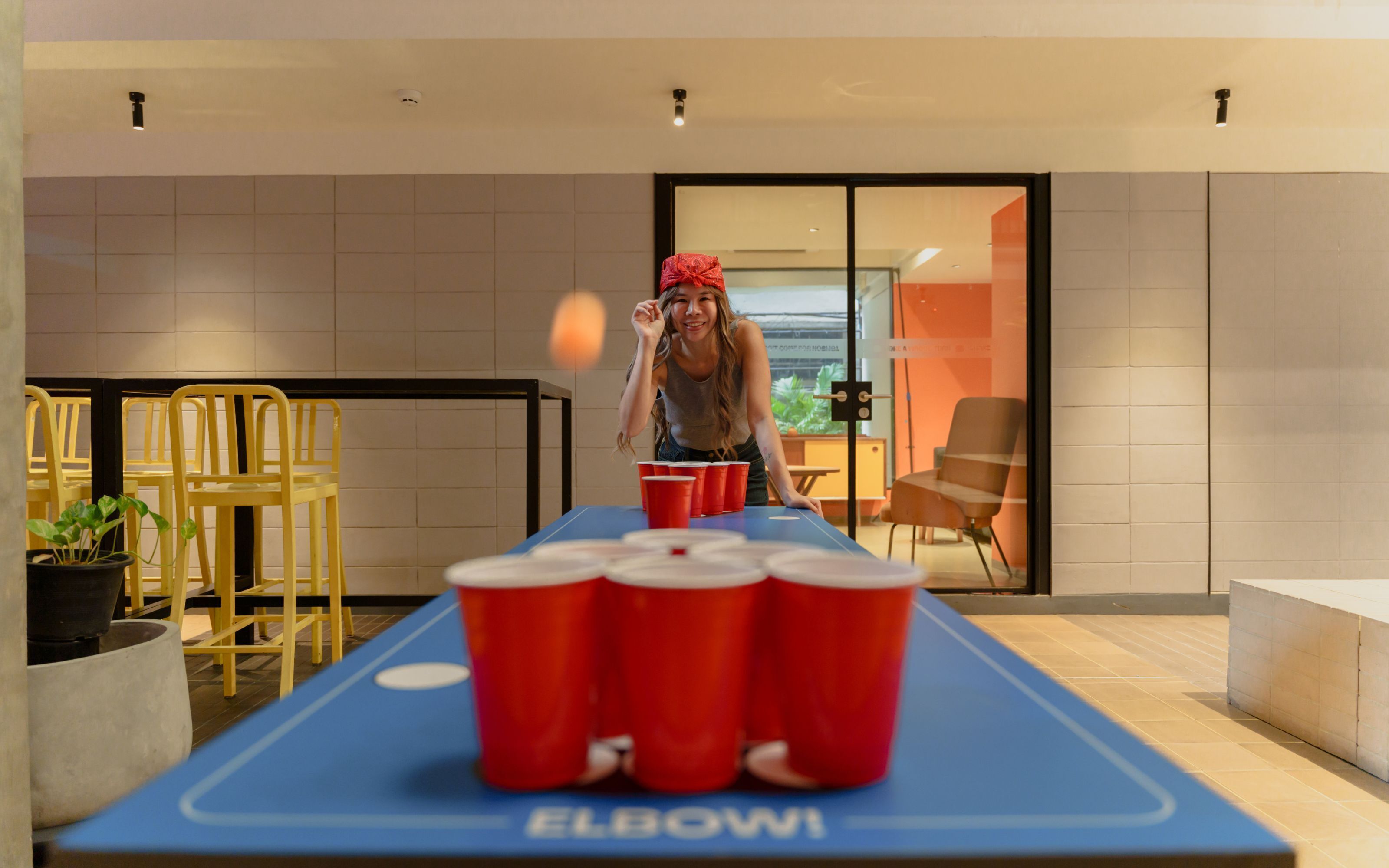 A ping pong table with red cups labeled "ELBOWI" and a person playing.