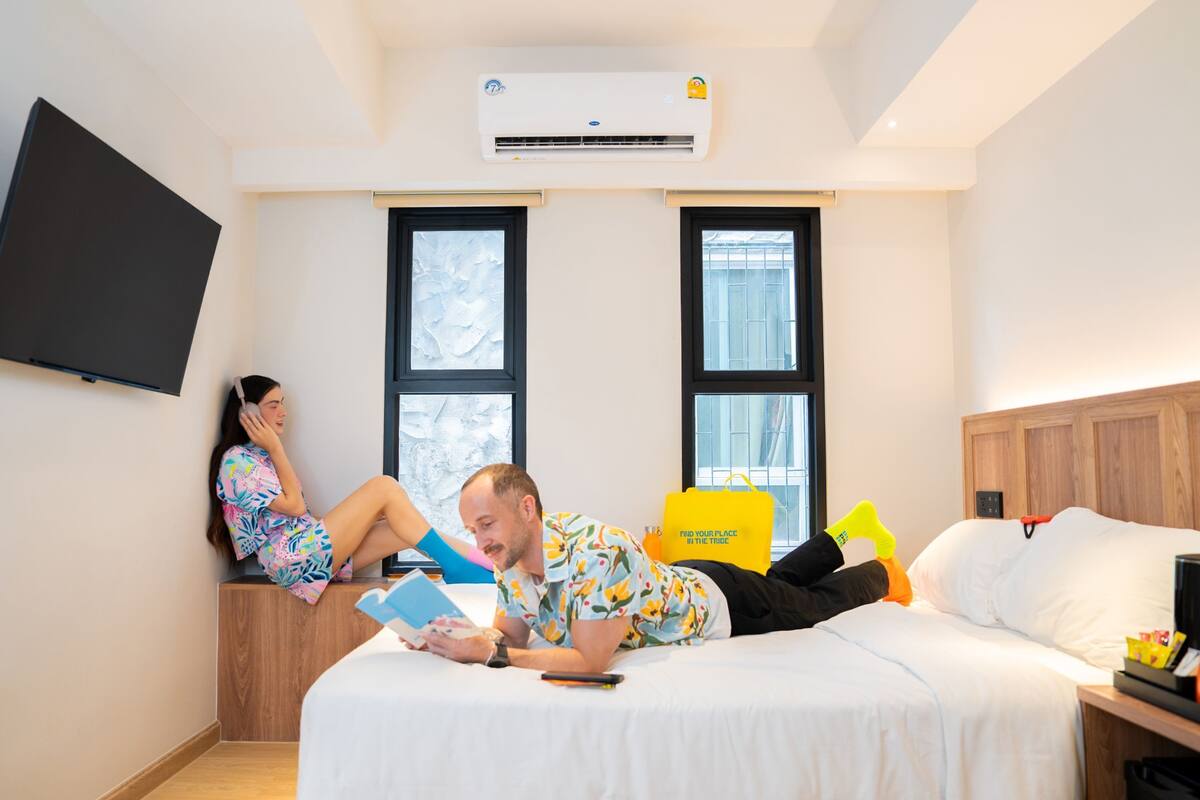 Hotellihuone, jossa on sänky, seinälle asennettu taulutelevisio ja kaksi ikkunaa.