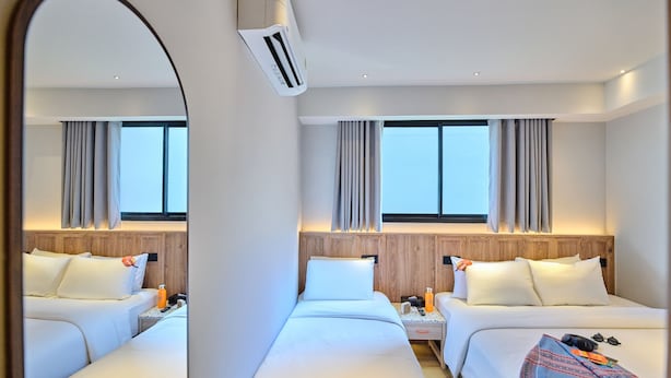 A hotel room with two beds, a wooden headboard, a nightstand, a mirror, and a window with curtains.