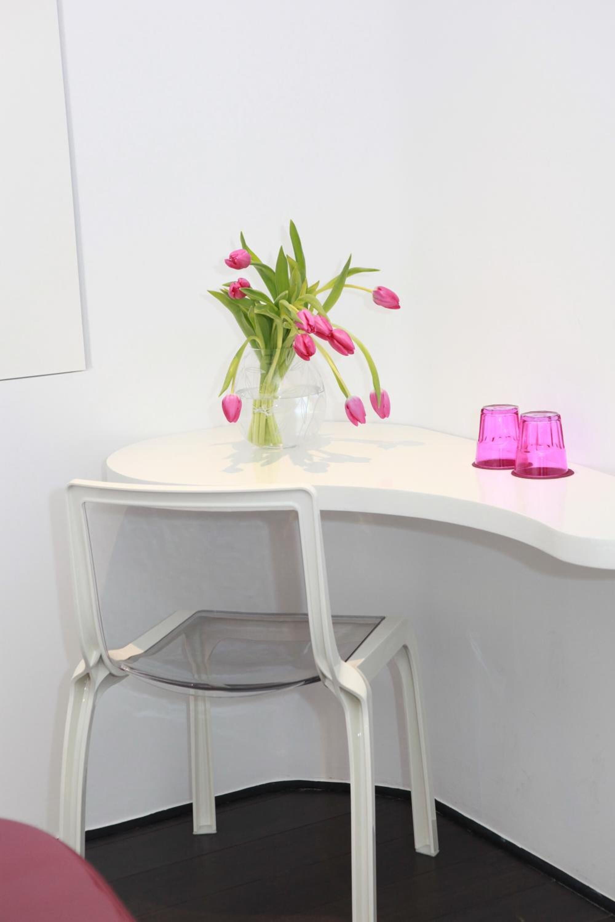 Een witte tafel met een vaas roze tulpen en twee roze glazen.