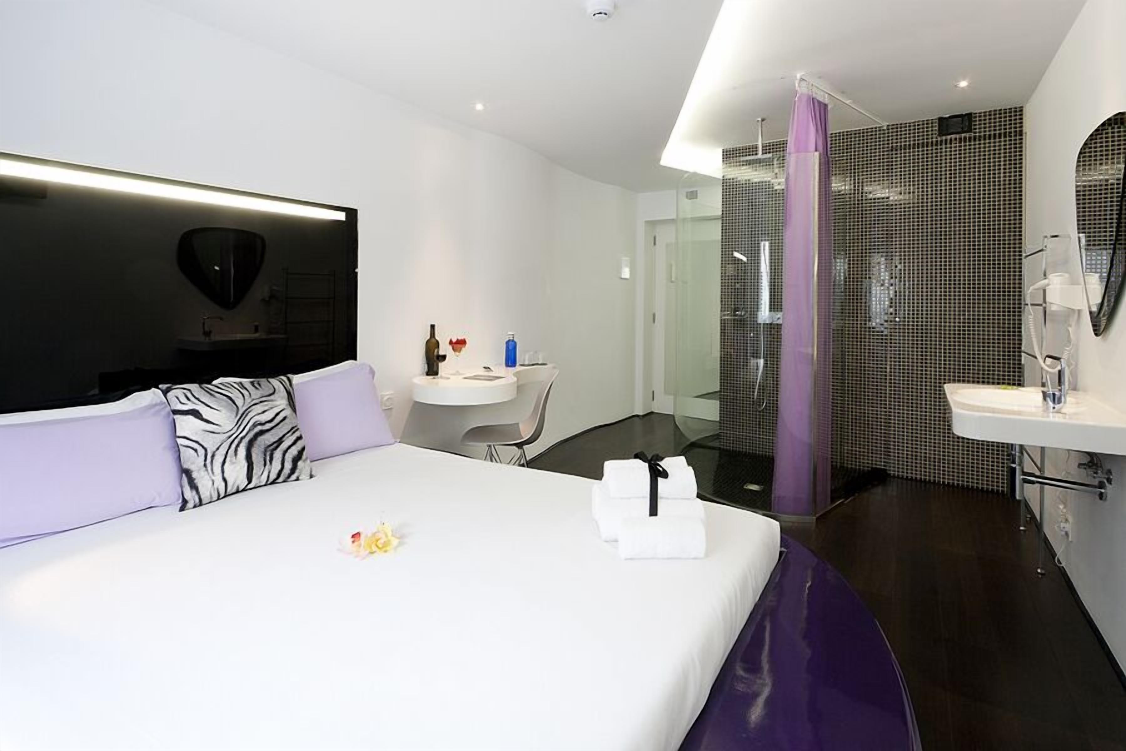 Een moderne hotelkamer met een groot bed, een klein bureau, een douche en een badkamer met wastafel en spiegel.