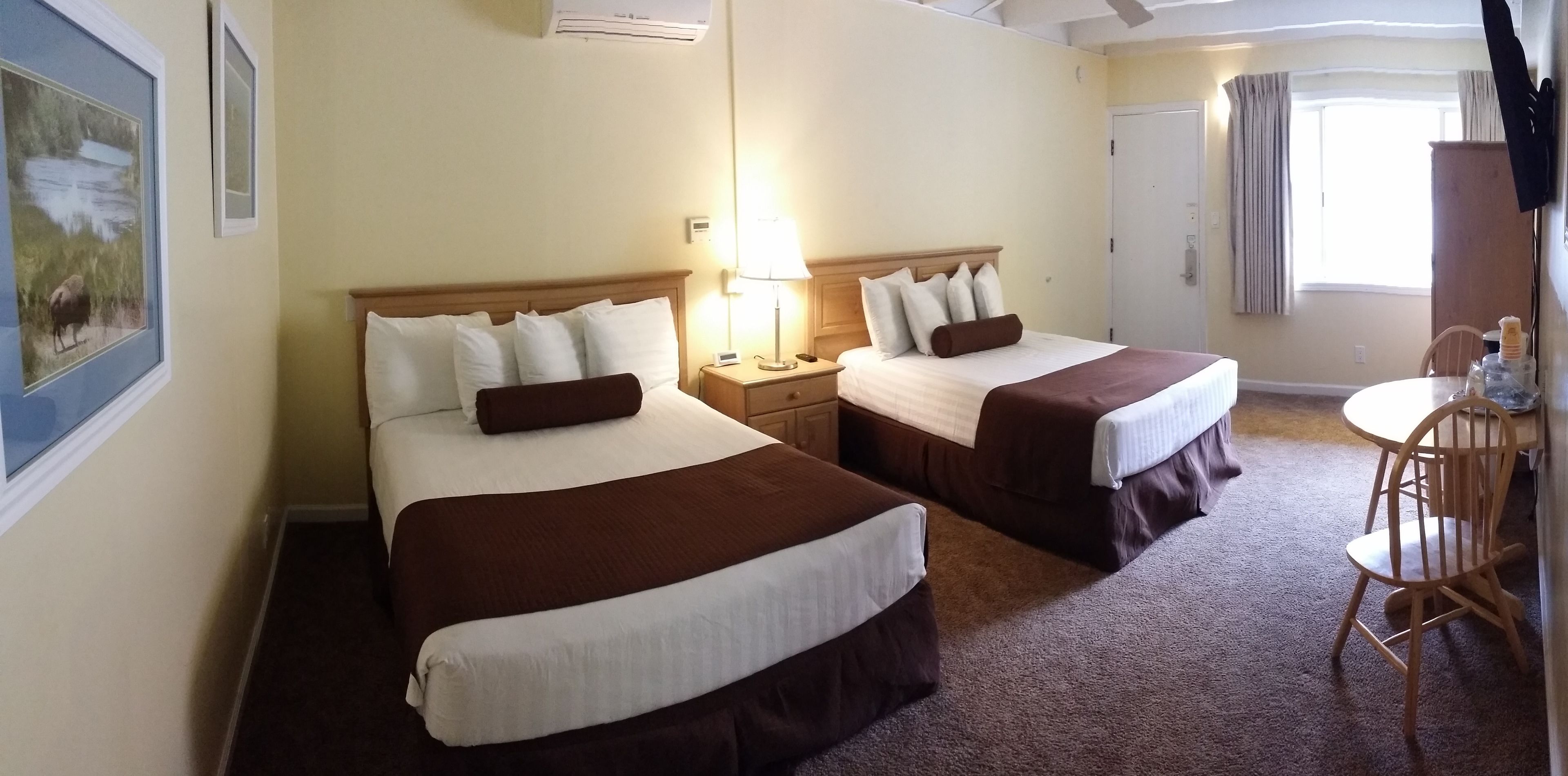 A hotel room with two beds, a small table, and a chair.