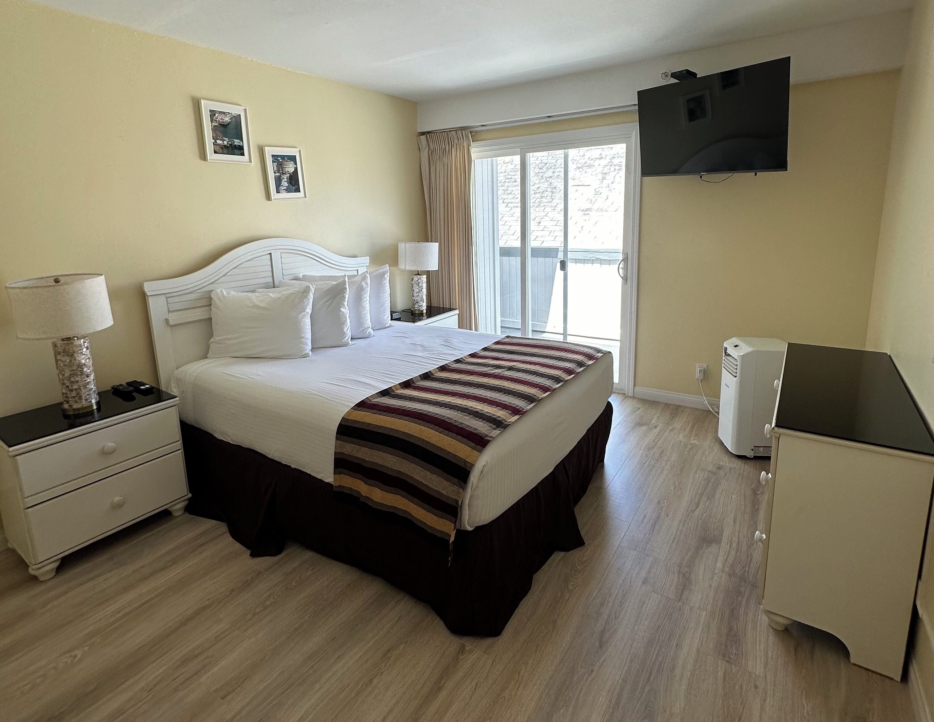 A hotel room with a bed, bedside tables, a TV, and a window with curtains.
